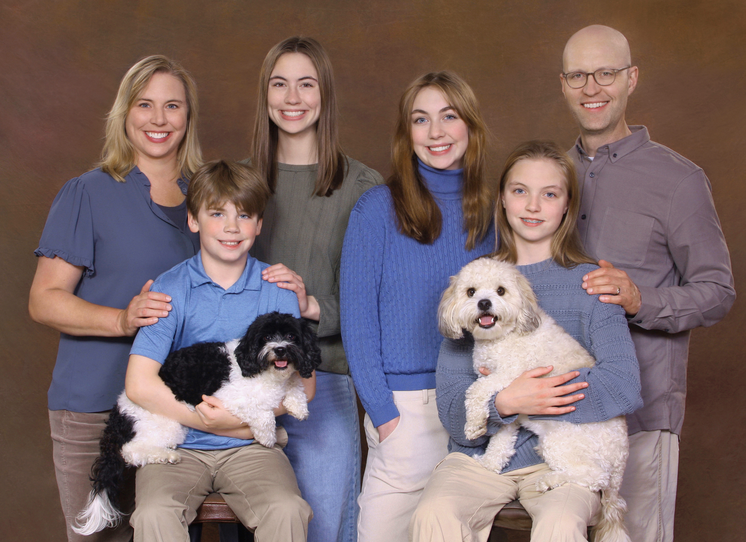 Tan background of a portrait studio, family of four including a chestnut golden retriever, smile for the camera.